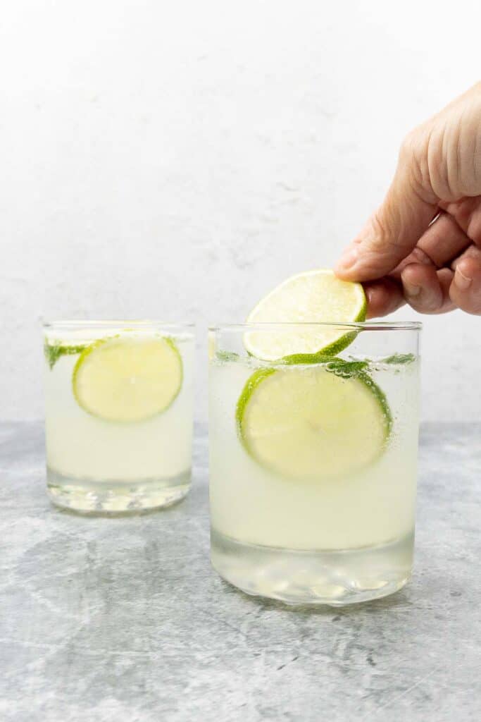Placing thin lime wheel on top of cocktail.