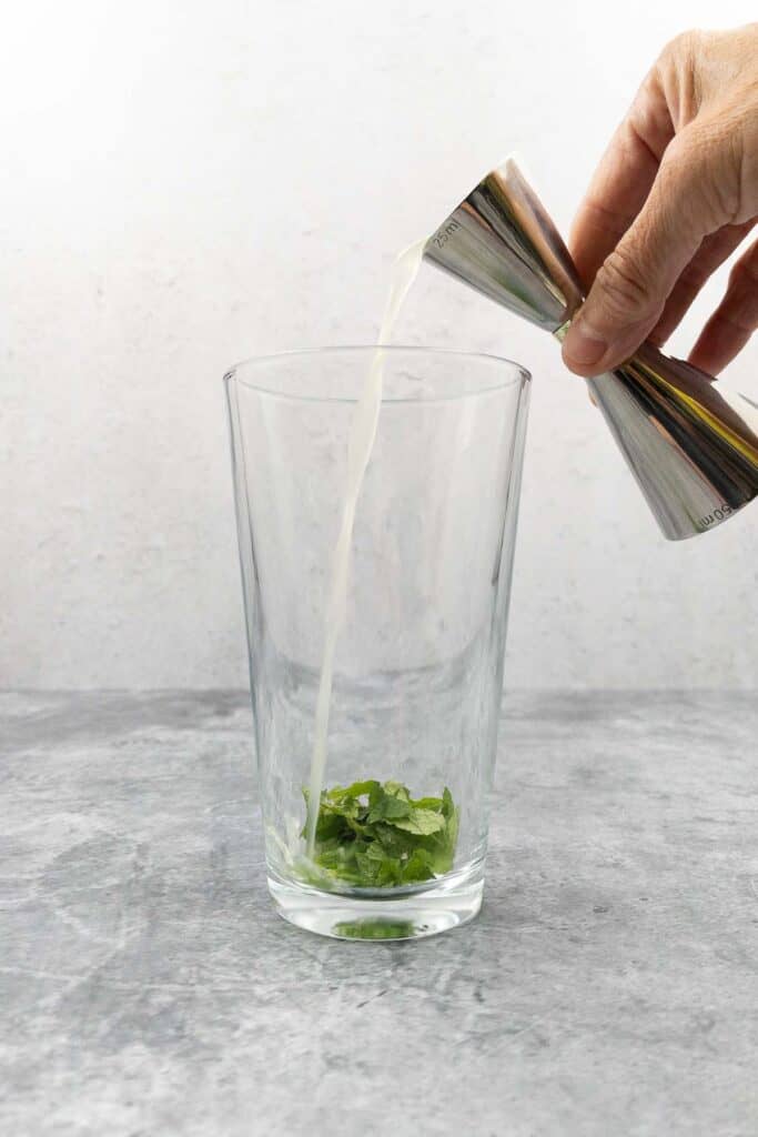 Adding lime juice to mint and sugar in a cocktail shaker.