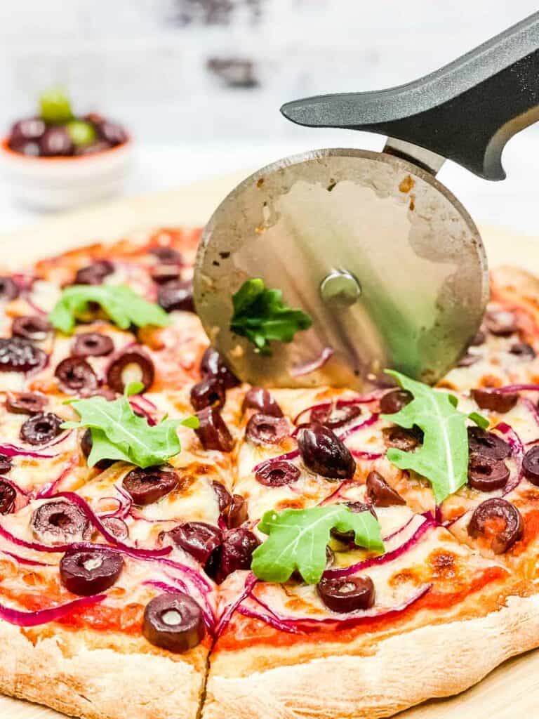 Someone using a pizza cutter to slice up pizza.