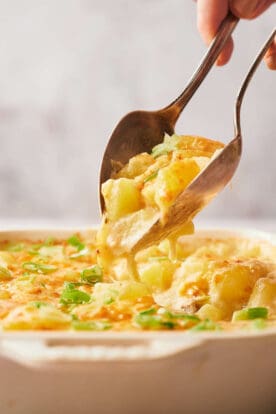 Someone dishing up a cheesy potato casserole.
