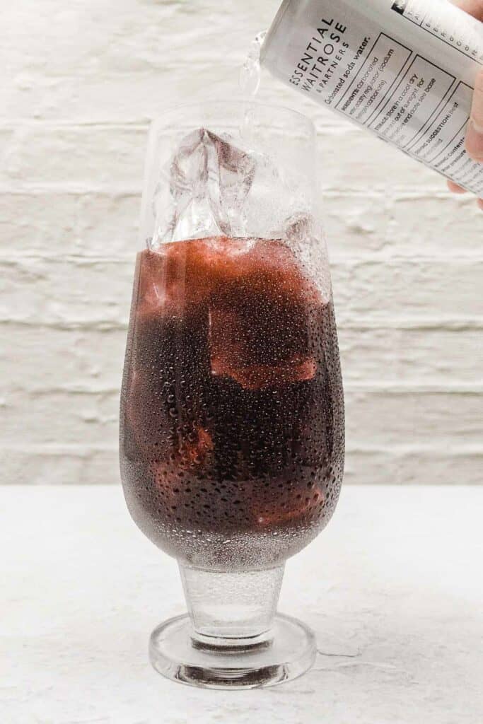 Topping the cocktail up with soda water.