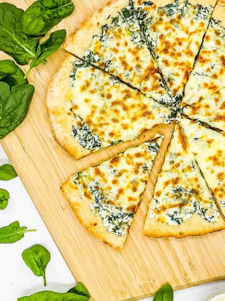 Spinach pizza, sliced and on a wooden peel.