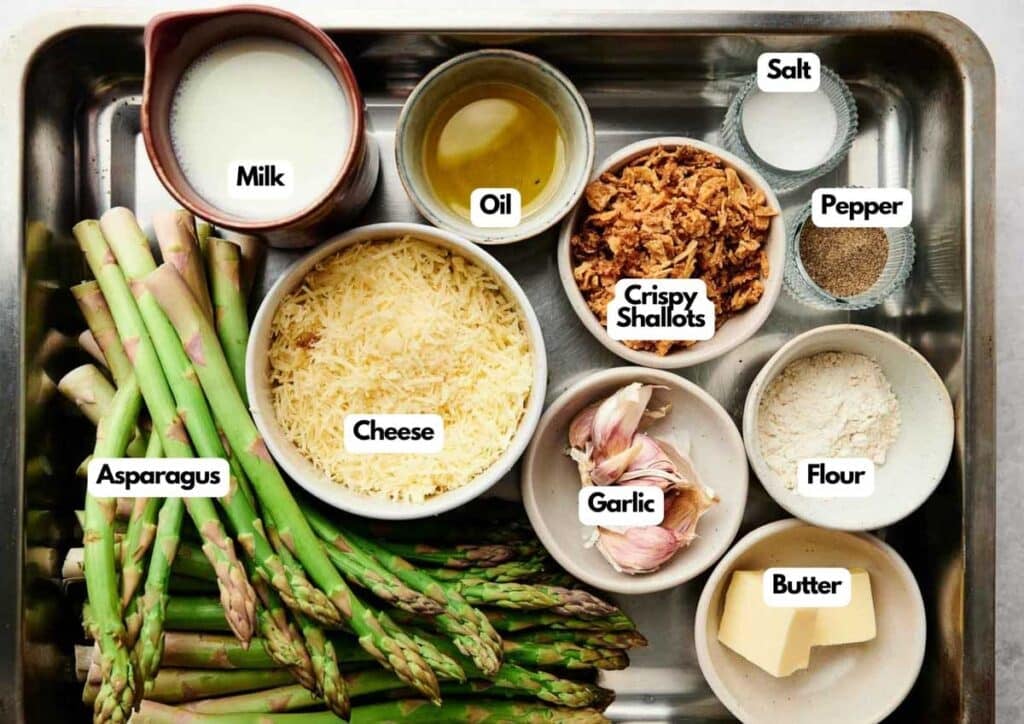 A tray with asparagus, milk, oil, cheese, crispy shallots, salt, pepper, flour, garlic cloves, and butter in separate bowls&mdash;everything you need for a delicious asparagus casserole.