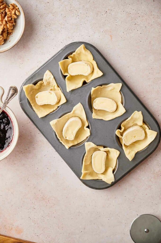 Dough placed in muffin tin with slices of brie on it.