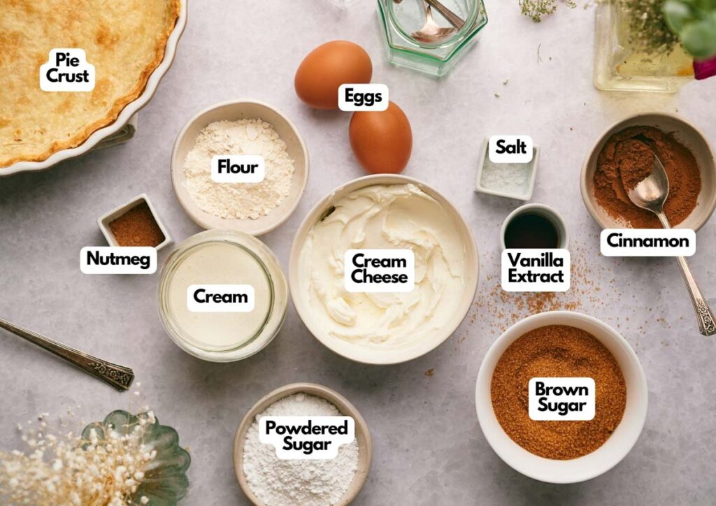 A flat-lay of labeled baking ingredients for Mississippi Mud Pie, including pie crust, flour, cream, cream cheese, powdered sugar, eggs, salt, vanilla extract, cinnamon, nutmeg, and brown sugar.