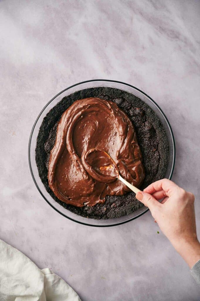 Someone spreading chocolate pudding payer on brownie layer.