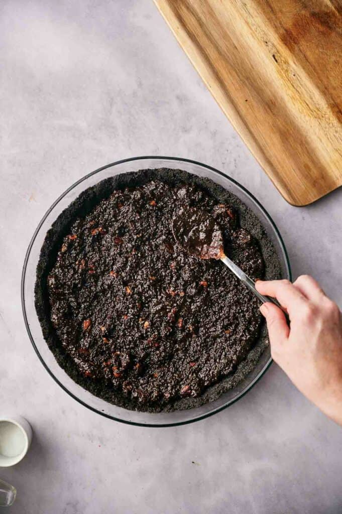 Someone spreading a brownie layer on an Oreo pie crust.