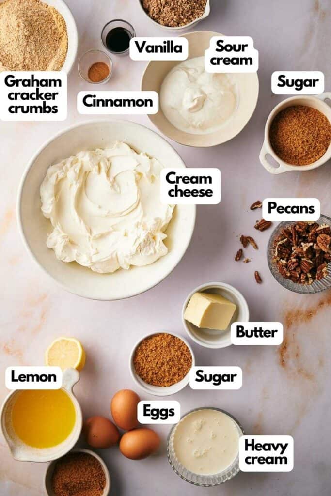 Ingredients needed, Graham cracker crumbs, cinnamon, vanilla, sour cream, sugar, pecans, cream cheese, unsalted butter, heavy cream, eggs, and lemon.