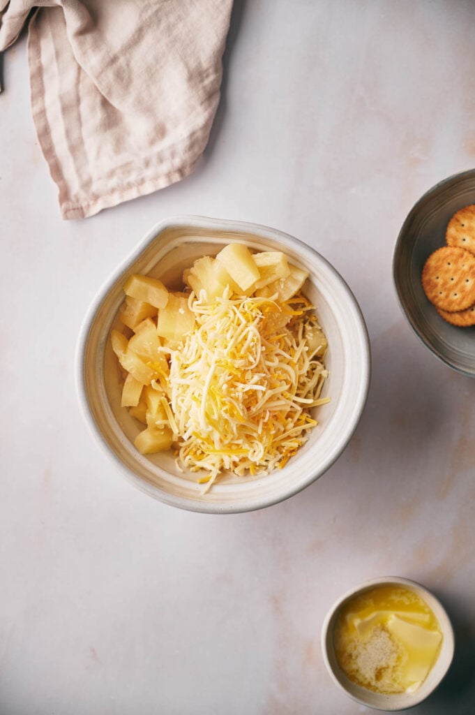 Shredded cheese added to the pineapple in a bowl.