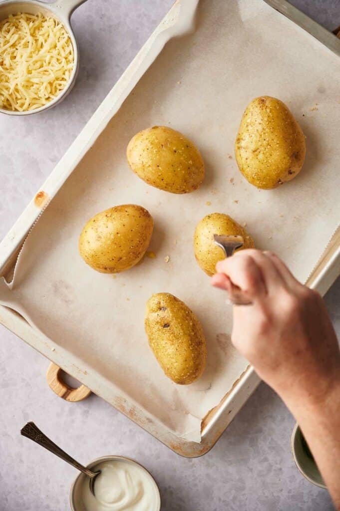 Someone using a fork to prick holes in the potatoes.