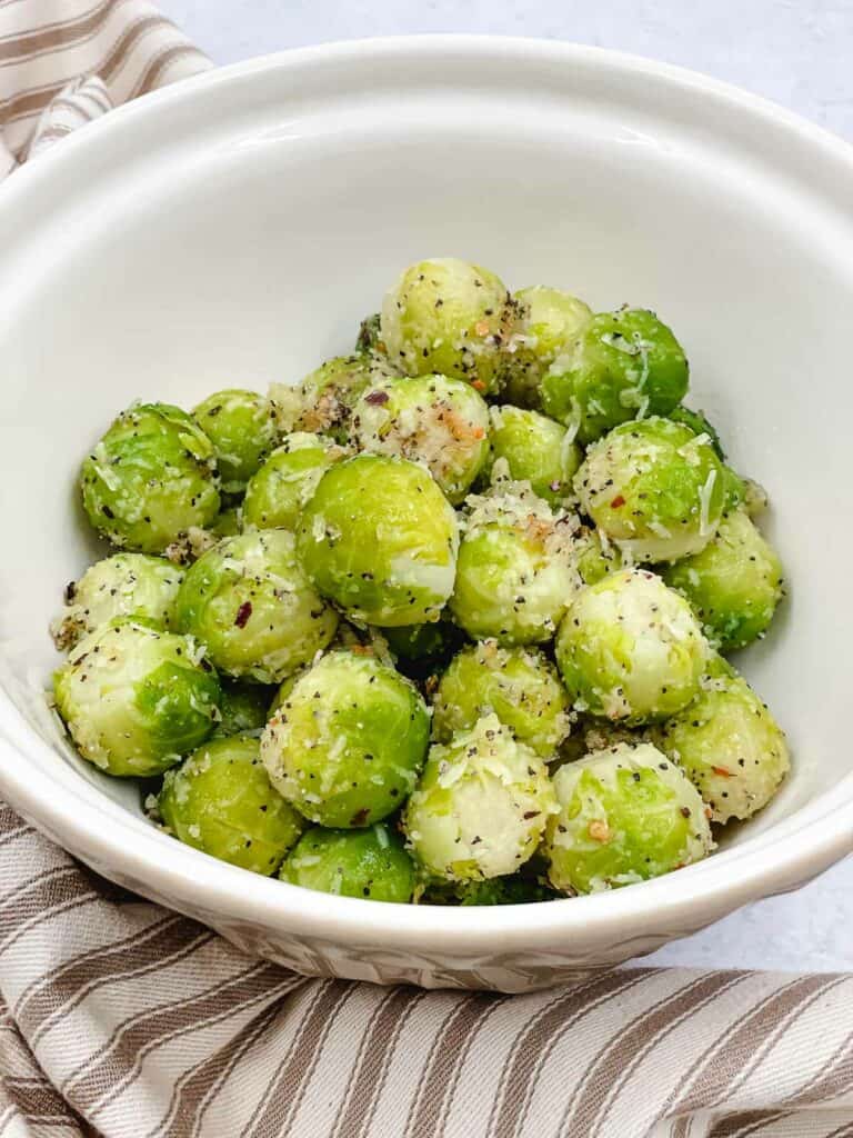 Uncooked Brussels sprouts in a mixing bowl with olive oil, red pepper flakes, garlic powder, and vegetarian Parmesan cheese coating them.