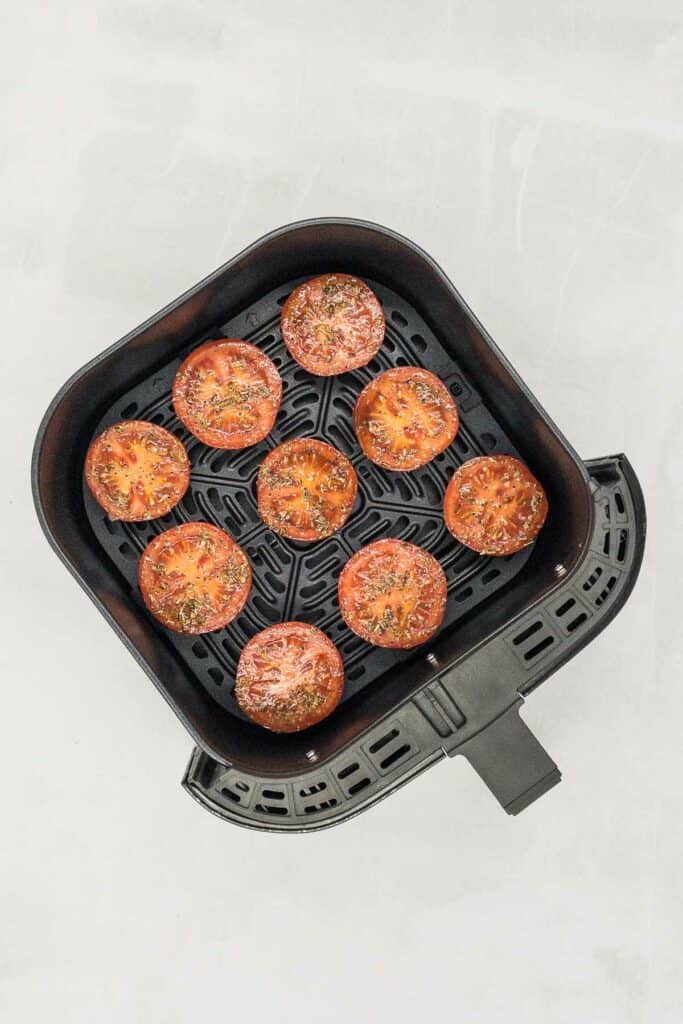 Red tomatoes marinated and placed in an air fryer basket.