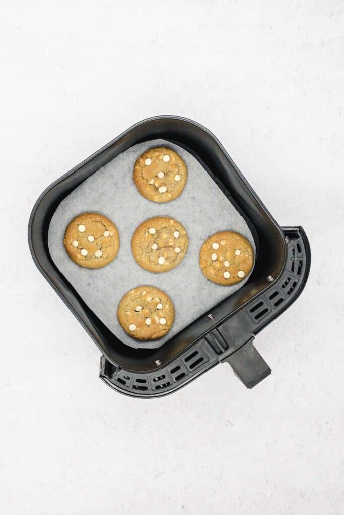 Baked white chocolate chip cookies in an air fryer basket.