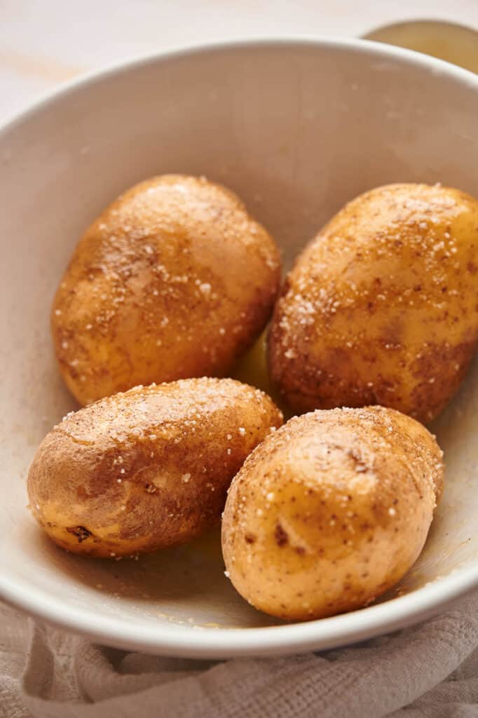 Russet potatoes in a bowl, coated with oil, salt, and pepper.