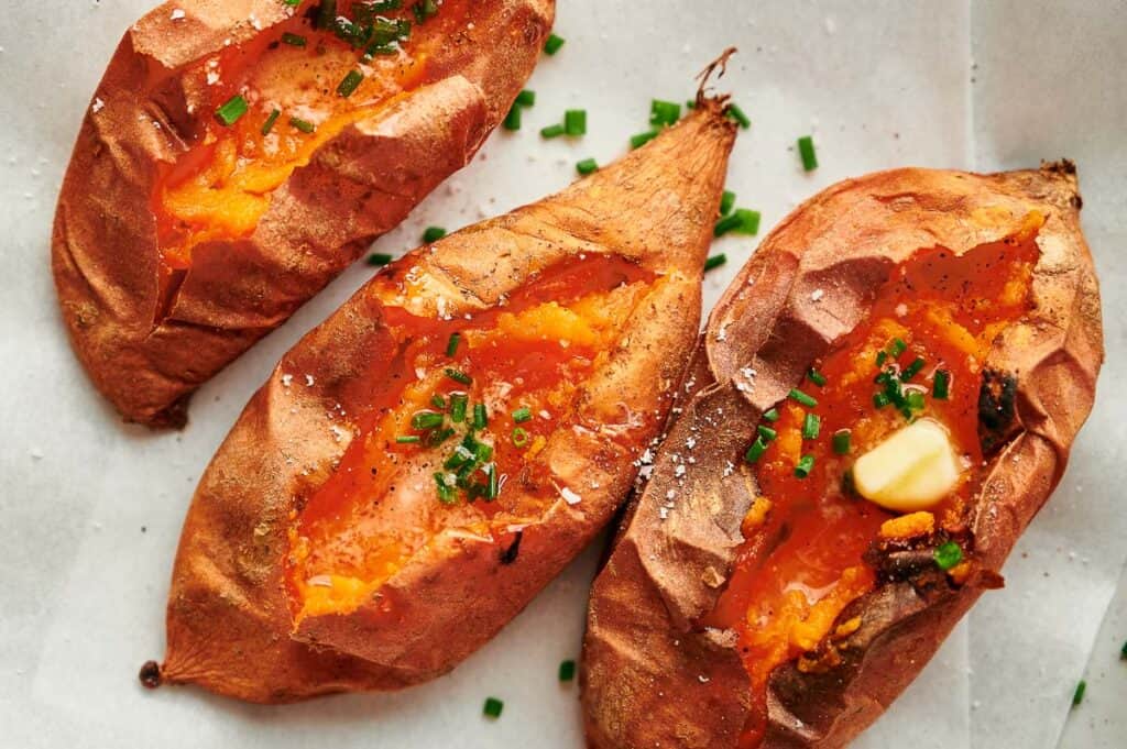 Baked sweet potatoes made in the air fryer with melted butter and chives in the middle of them.