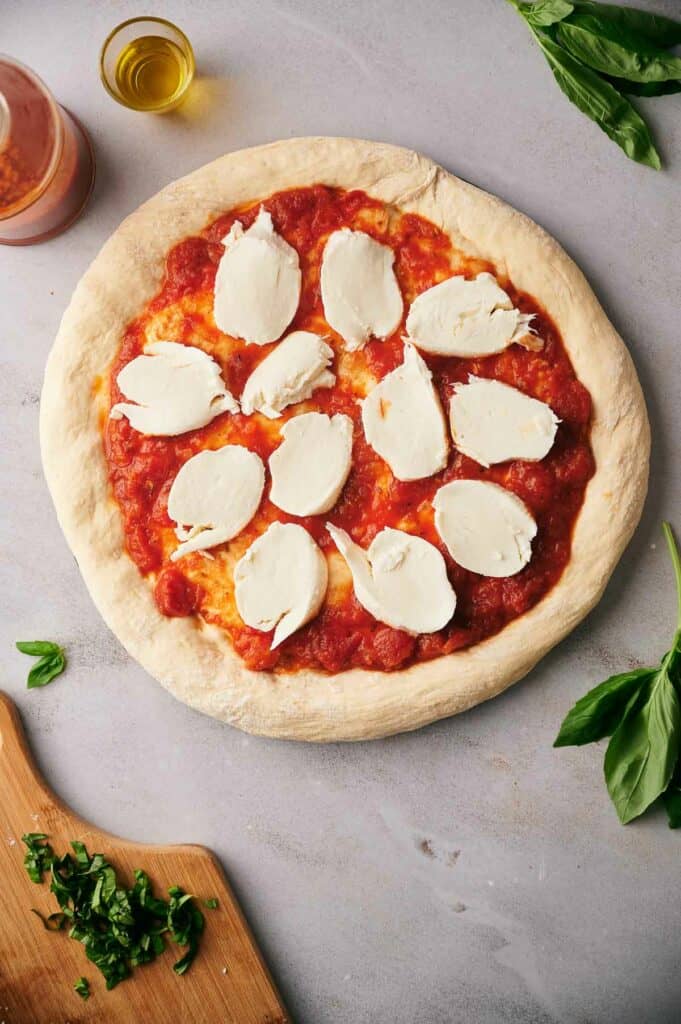 Buffalo mozzarella cheese slices on pizza sauce.
