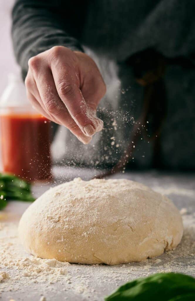 Someone scattering tipi flour on homemade pizza dough.