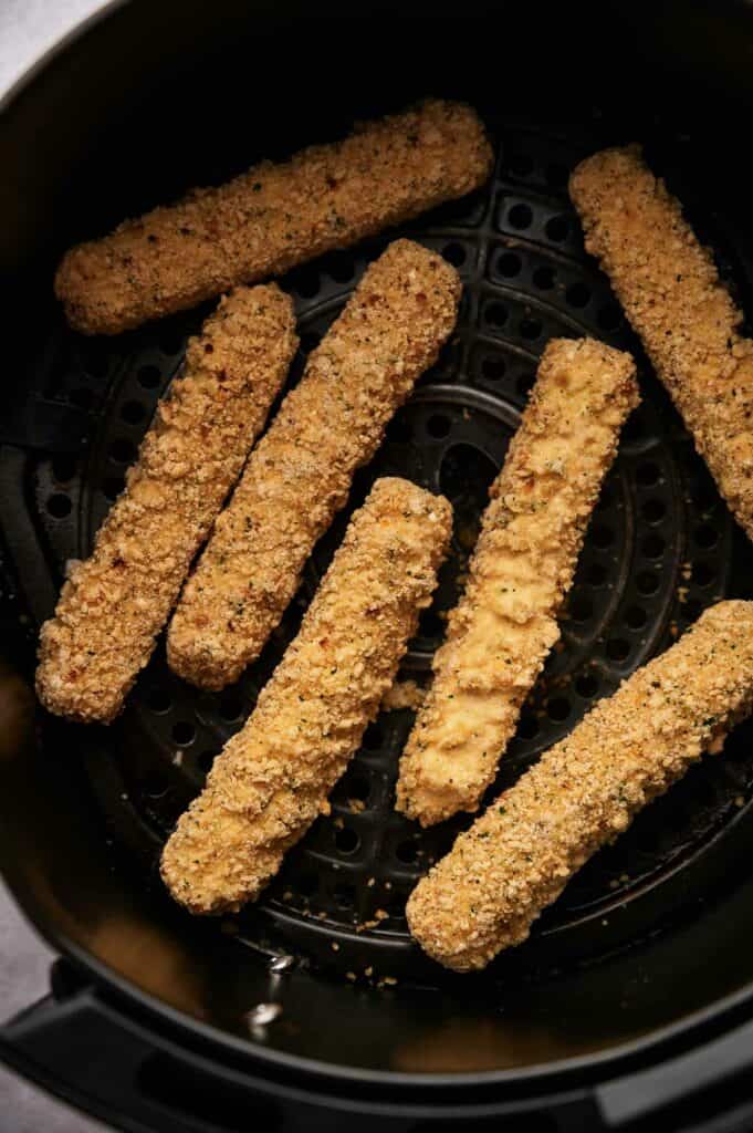 Uncooked mozzarella sticks in an air fryer basket.