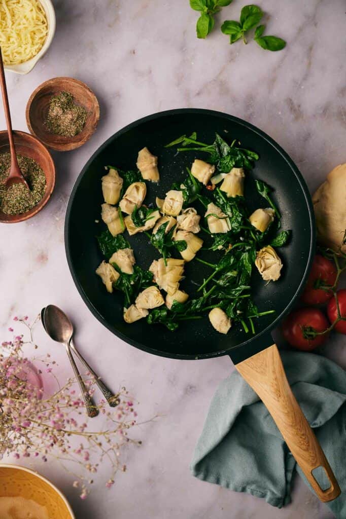 Marinated artichoke hearts added to a skillet.