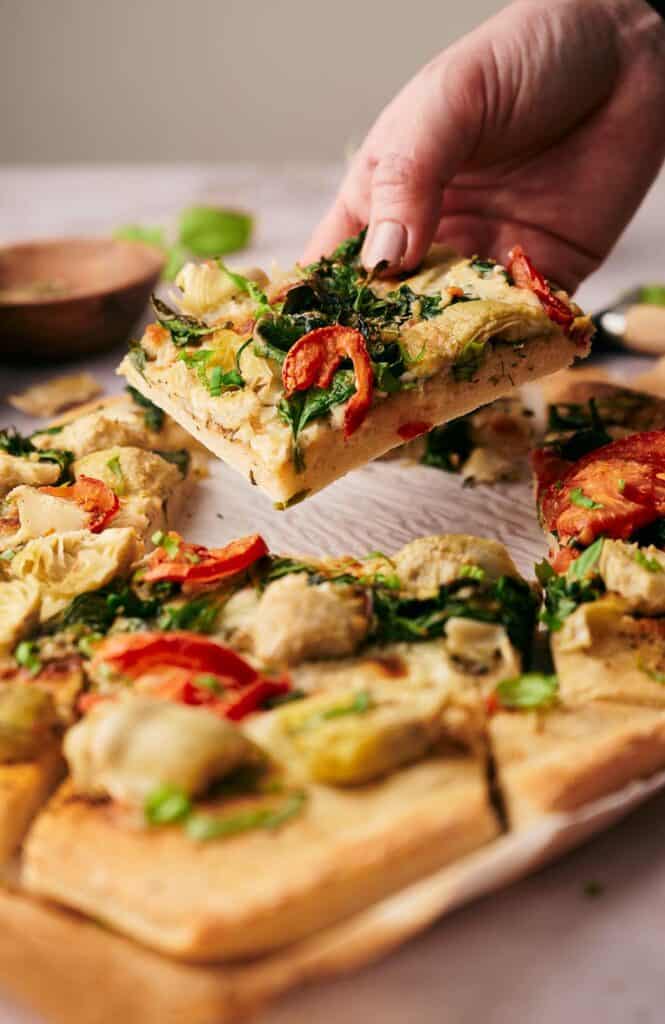 Someone grabbing a slice of artichoke pizza.