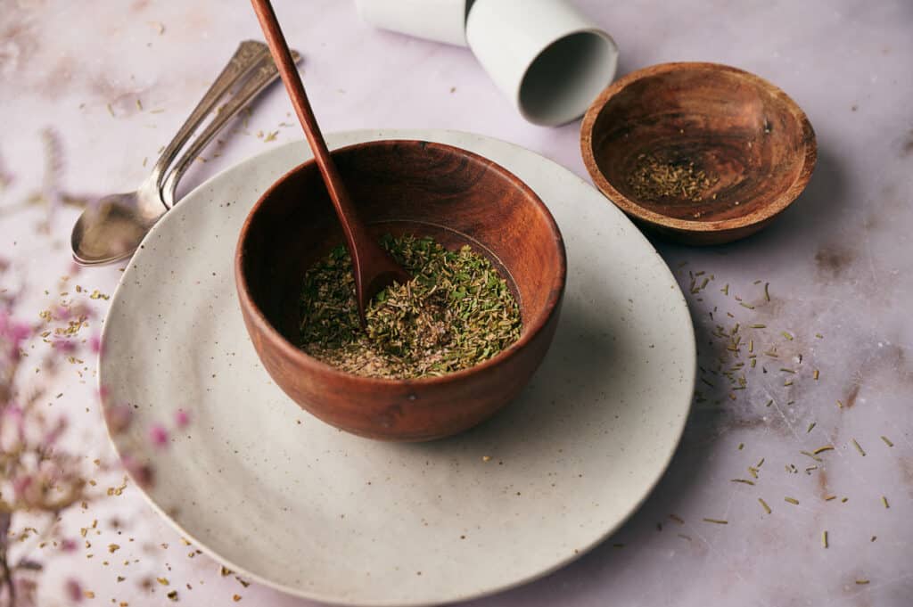 Pizza seasoning blend in a mixing bowl with a wooden spoon in it.