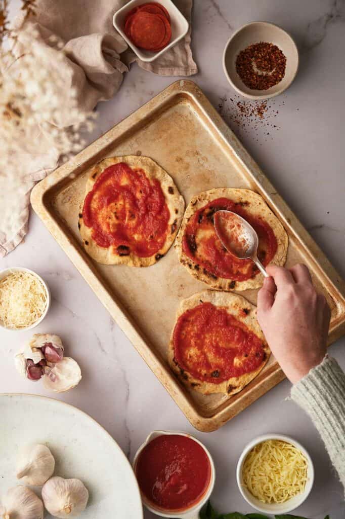 Spreading pizza sauce onto the tortillas.
