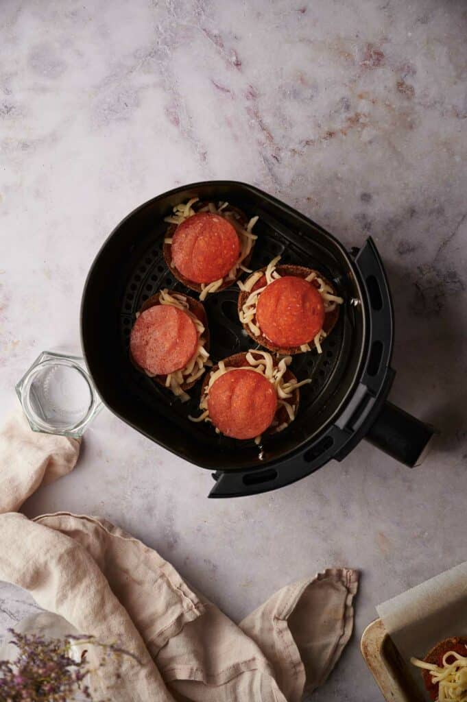 Uncooked pizza bagel bites in air fryer basket.
