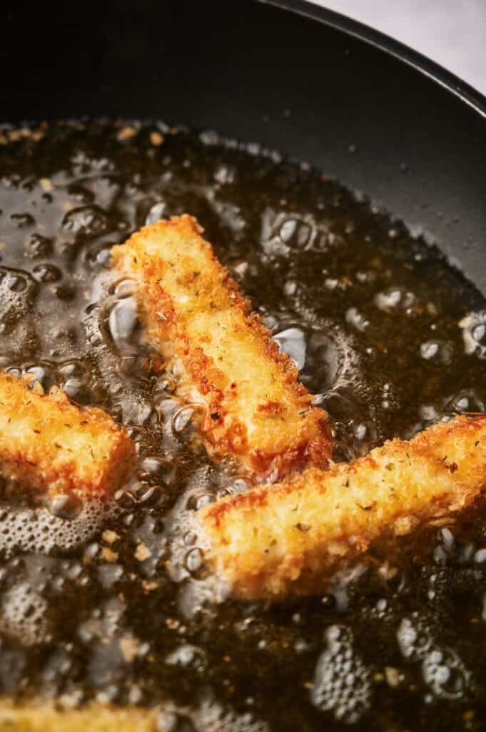 Mozzarella cheese sticks being deep fried.