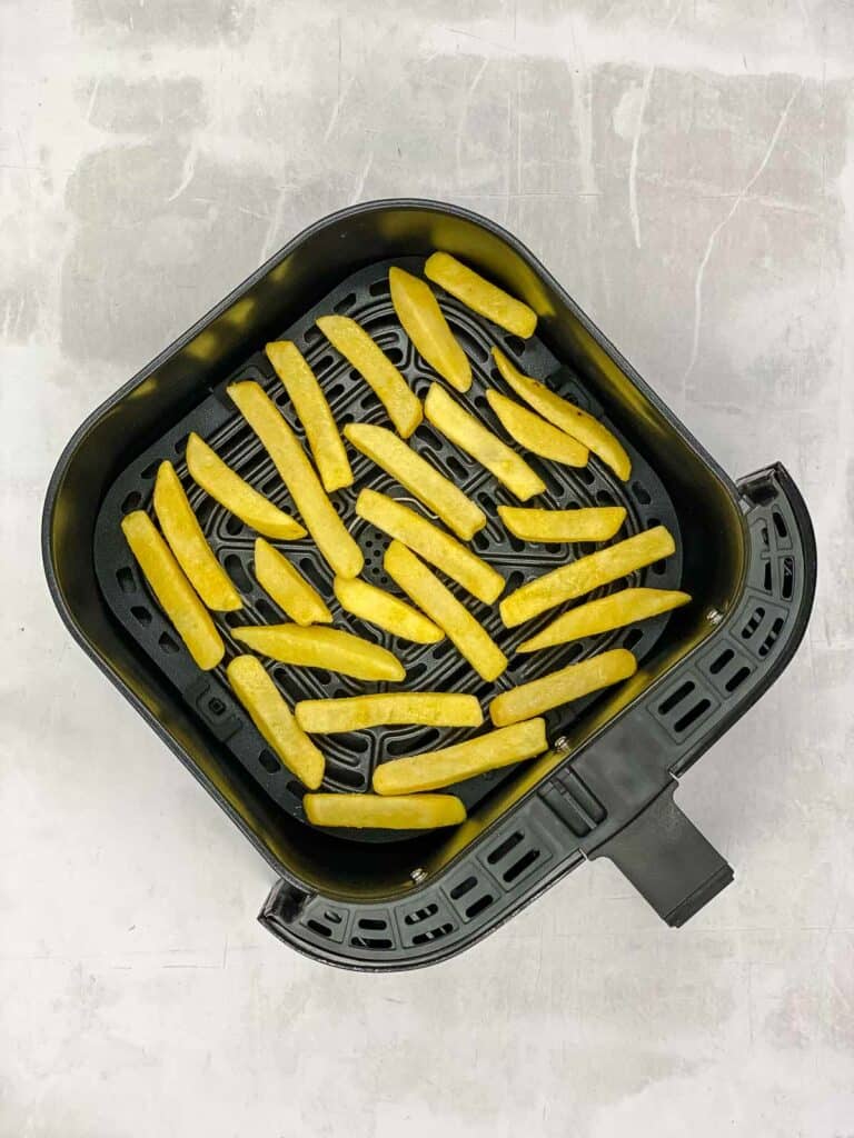 Frozen fries in an air fryer basket.