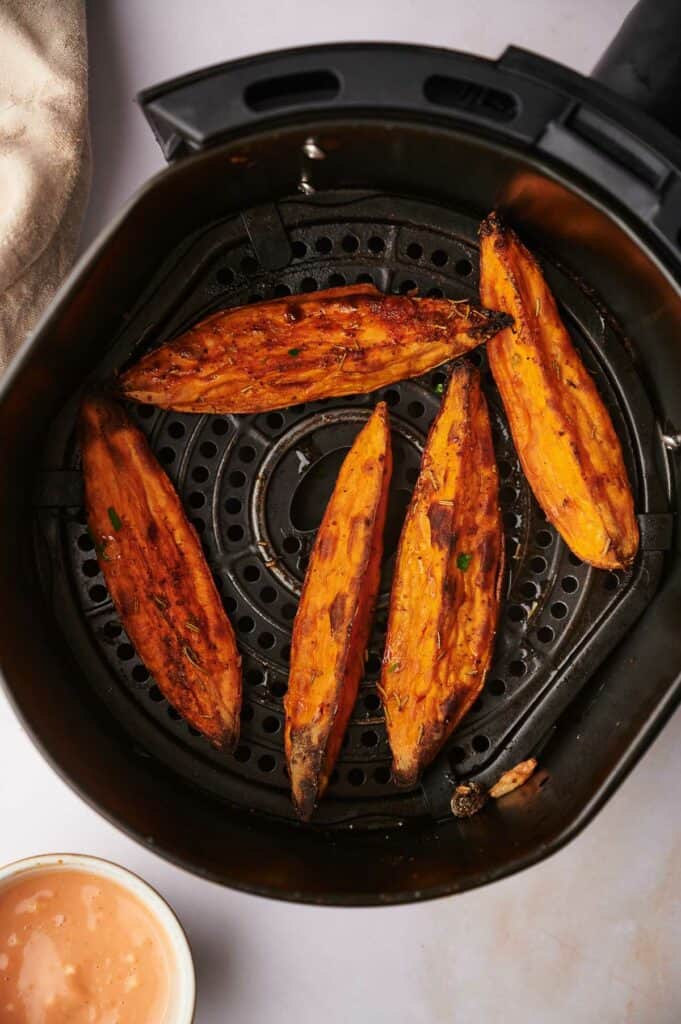 Cooked sweet potato wedges in air fryer basket.