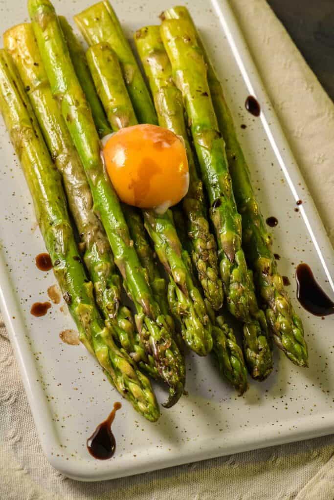 Asparagus cooked with egg served on a white ceramic tray on the table.