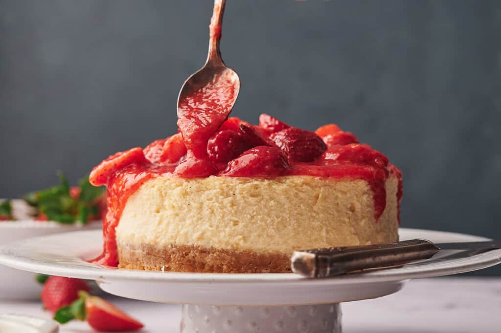 Drizzling strawberry topping over a baked cheesecake.
