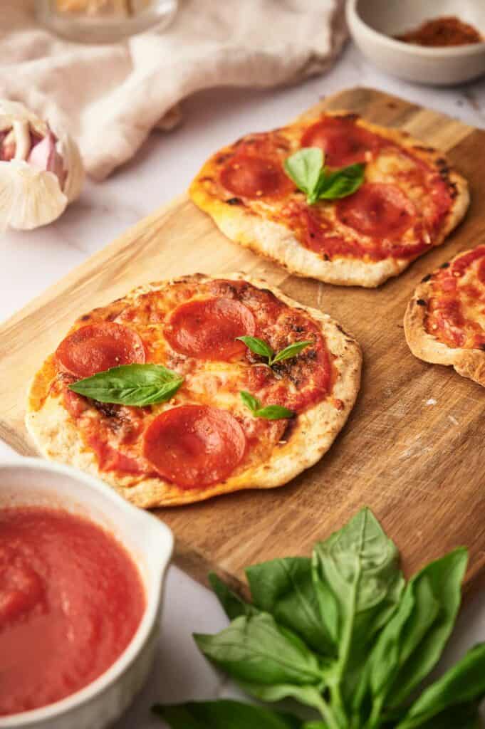 Cooked tortilla pizza on a chopping board, with fresh basil leaves.