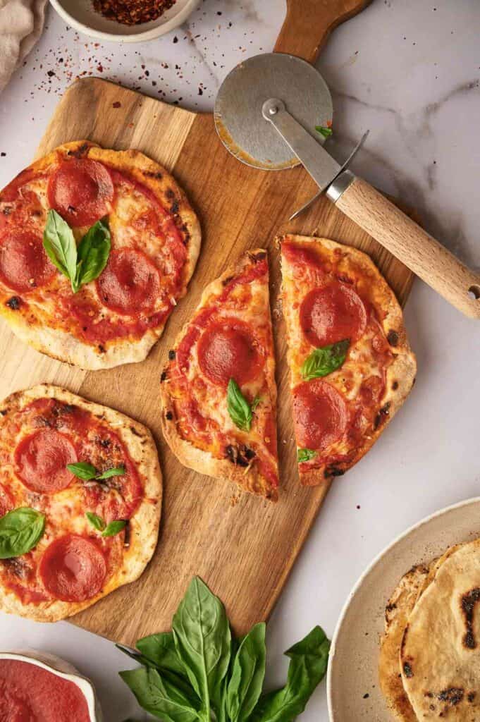 Sliced pizza on a chopping board with a pizza cutter.