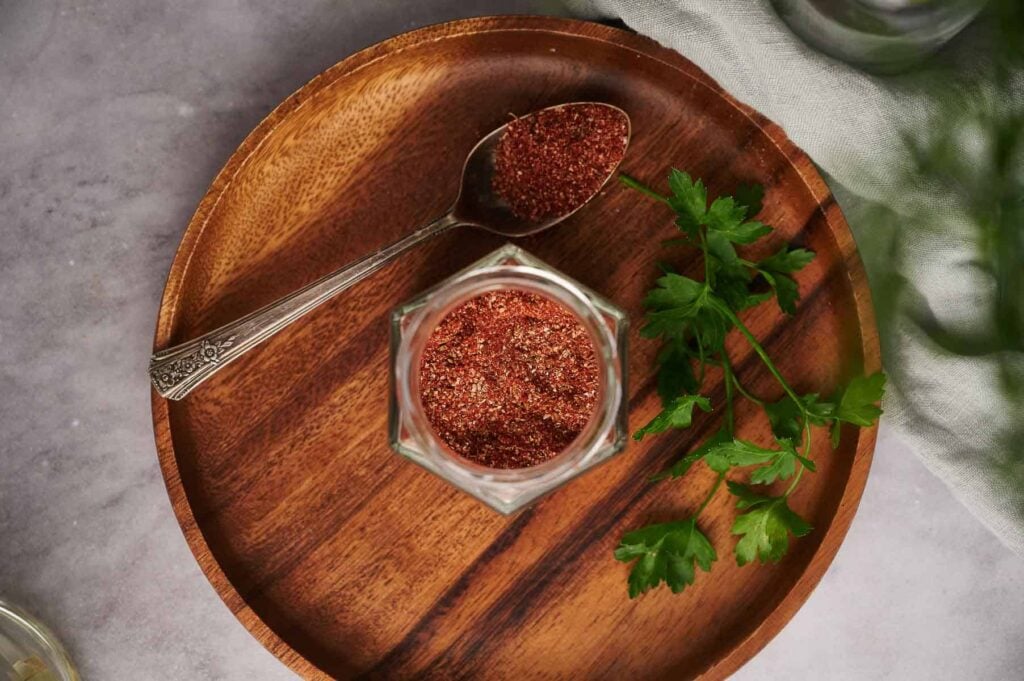 Homemade burrito seasoning mix in a glass jar and on a teaspoon.