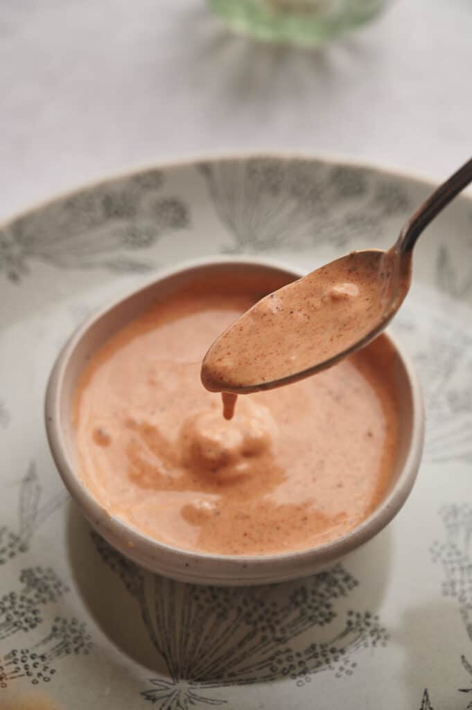 A spoon with sweet potato dip dripping off it over a bowl of sauce.
