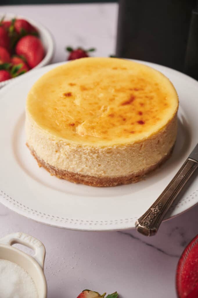 Air fryer cheesecake on a plate with a knife and other ingredients around it.