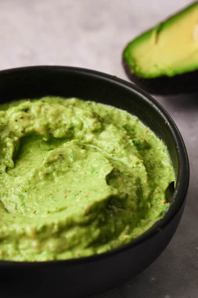 A bowl of freshly made avocado sauce with an avocado by it's side.