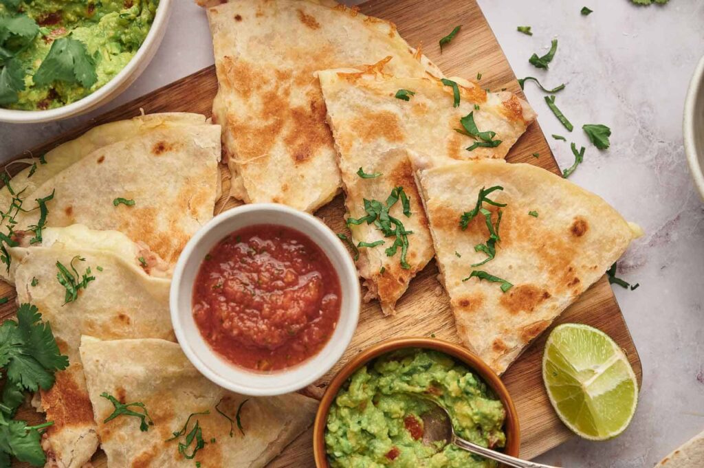 Delicious cheese quesadilla sliced and ready to eat with a salsa and guacamole dip.