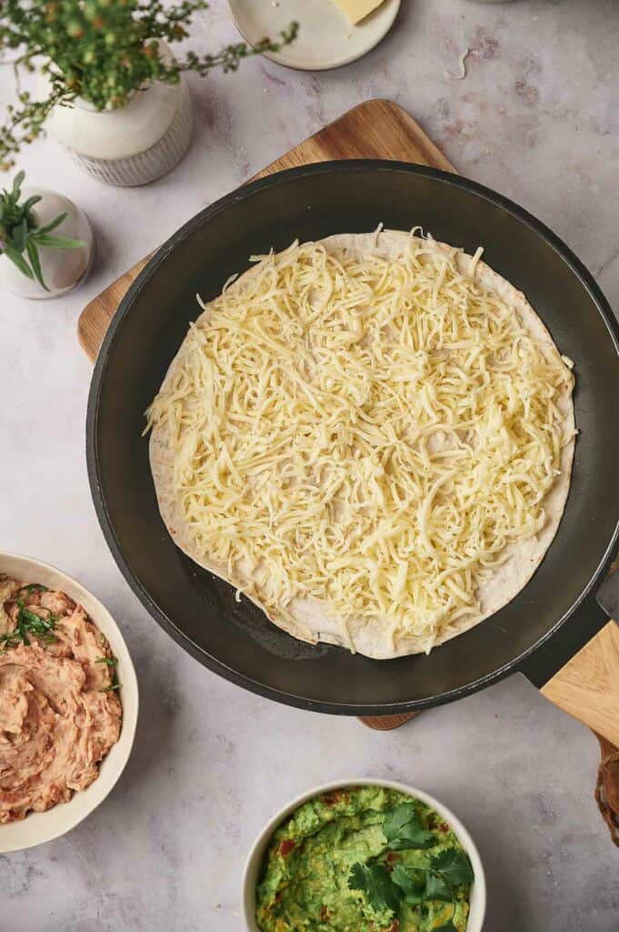 An uncooked tortilla with pr shredded cheese on top.