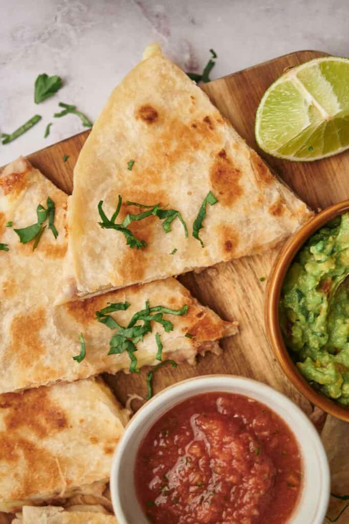 Tasty cheese quesadilla sliced with tomato salsa, guacamole and a slice of lime.