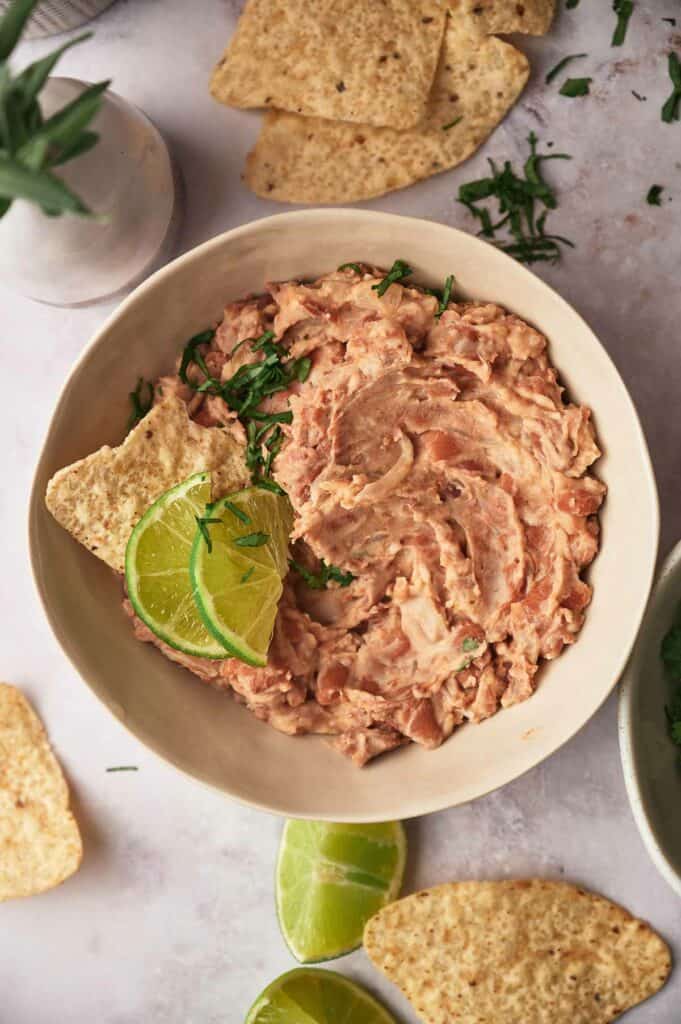 Homemade refried beans in a serving bowl with slices of lime and tortilla chips.