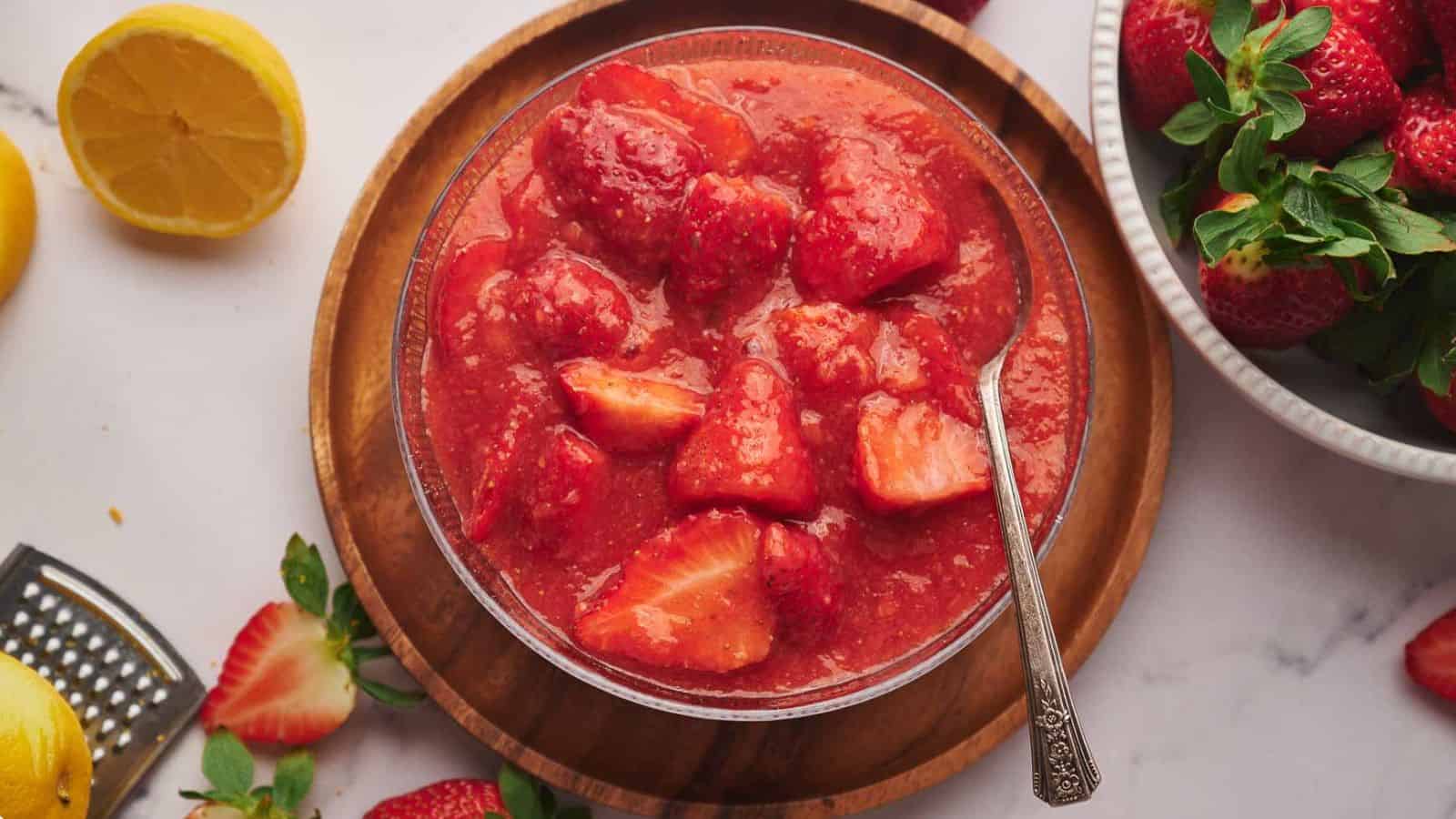 A bowl of strawberry sauce with lemon slices and a spoon.