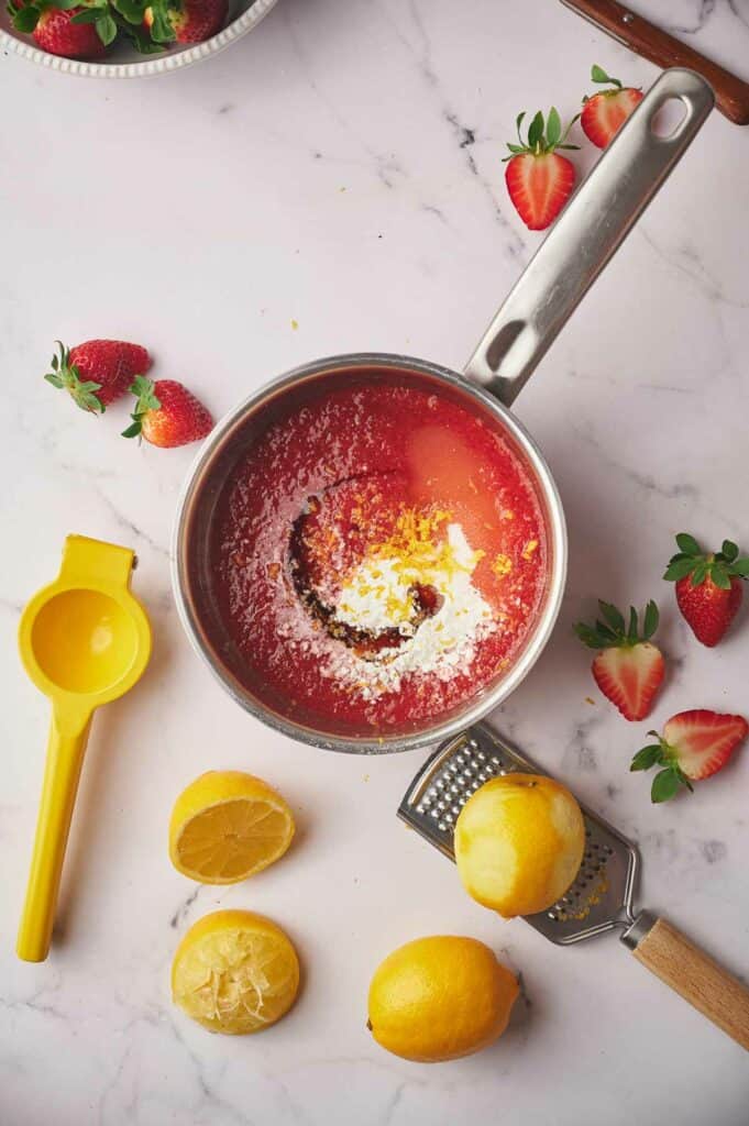 Ingredients in a pan, with lemons and strawberry halves around the pan.
