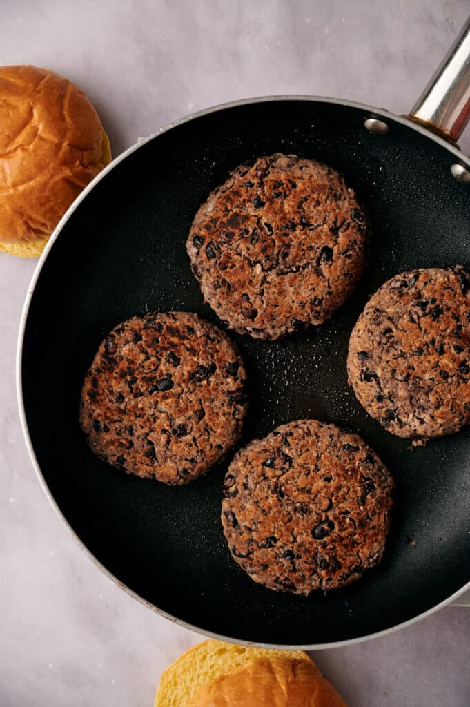 Four black bean burgers cooking in a skillet.