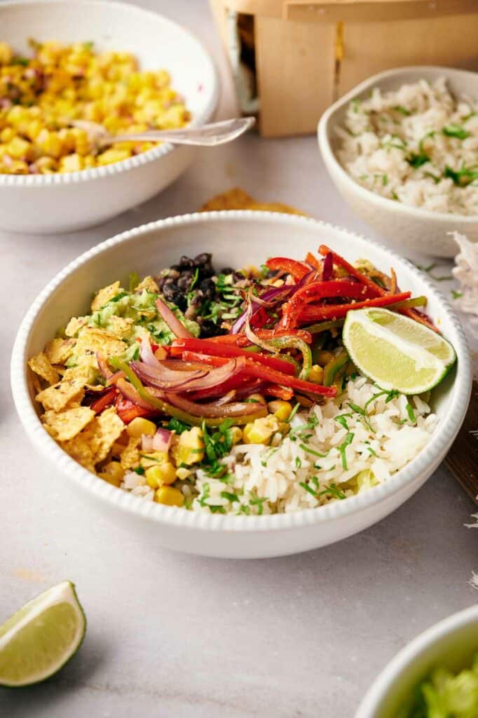 A healthy burrito bowl surrounded by bowls of ingredients.