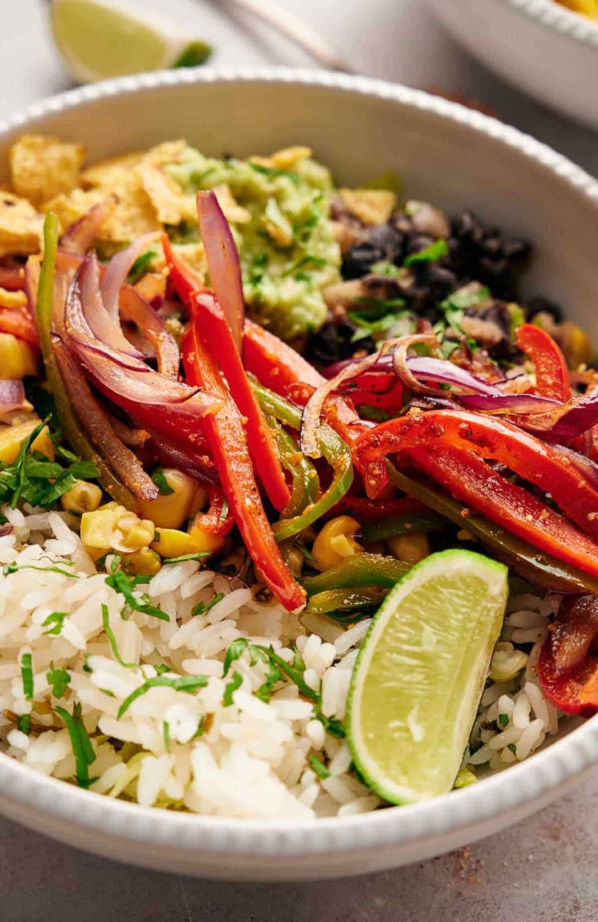 Fajita vegetables sit on top of a burrito bowl with rice, tortillas, and corn salsa.
