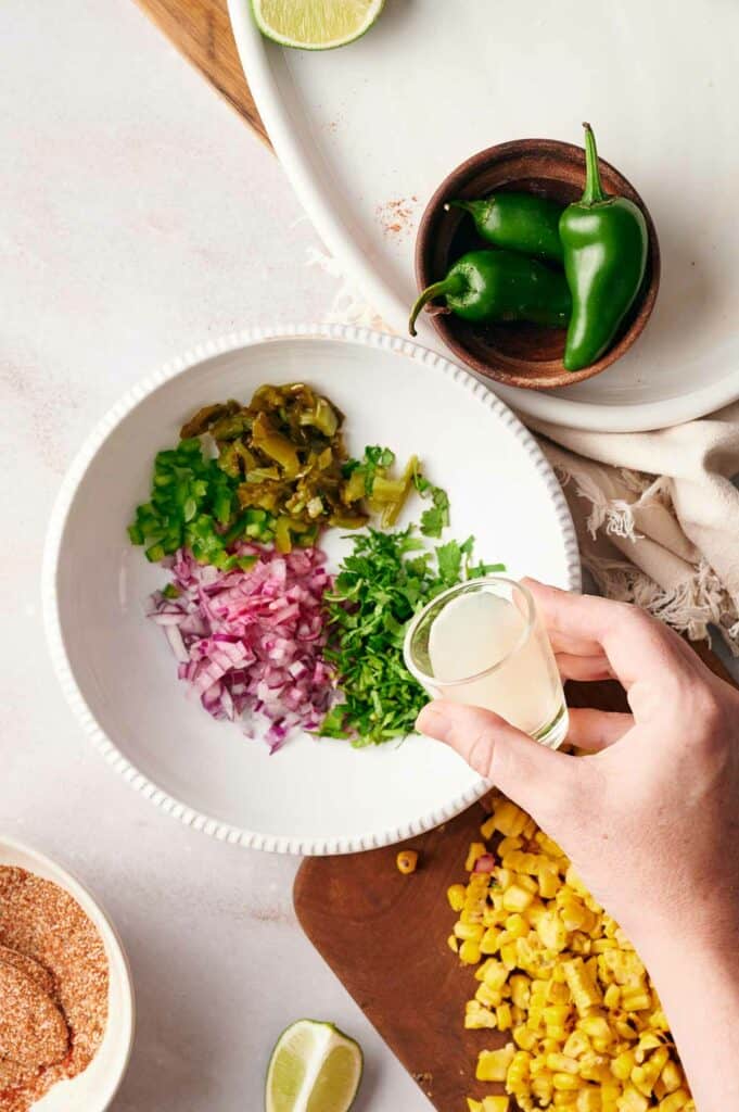 Someone adding lemon juice to the ingredients that are in a mixing bowl, with spicy peppers in a bowl nearby.