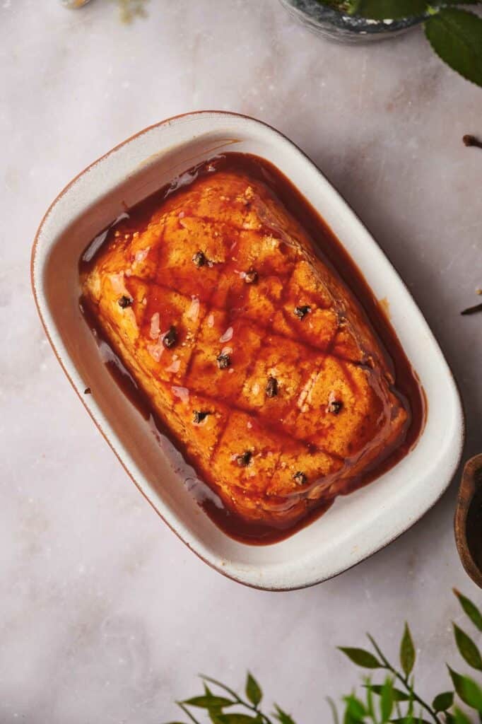 Vegan ham in a baking dish with glaze poured over it.