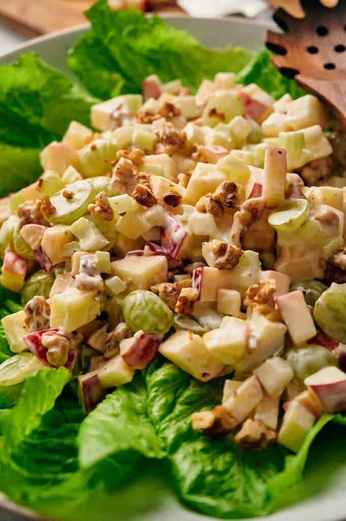 A close up of the Waldorf Salad in a white bowl, and wooden serving spoons.